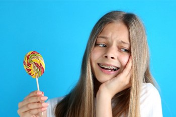 Young girl with braces regretting biting into a rainbow colored lollipop 