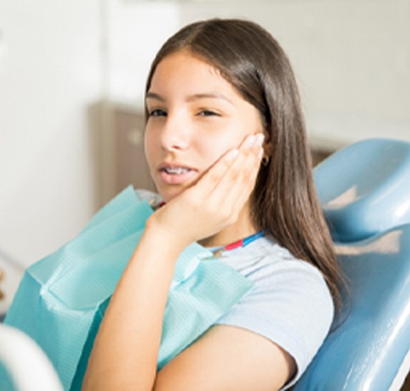 teenage girl with braces sitting in examination chair holding her cheek in pain